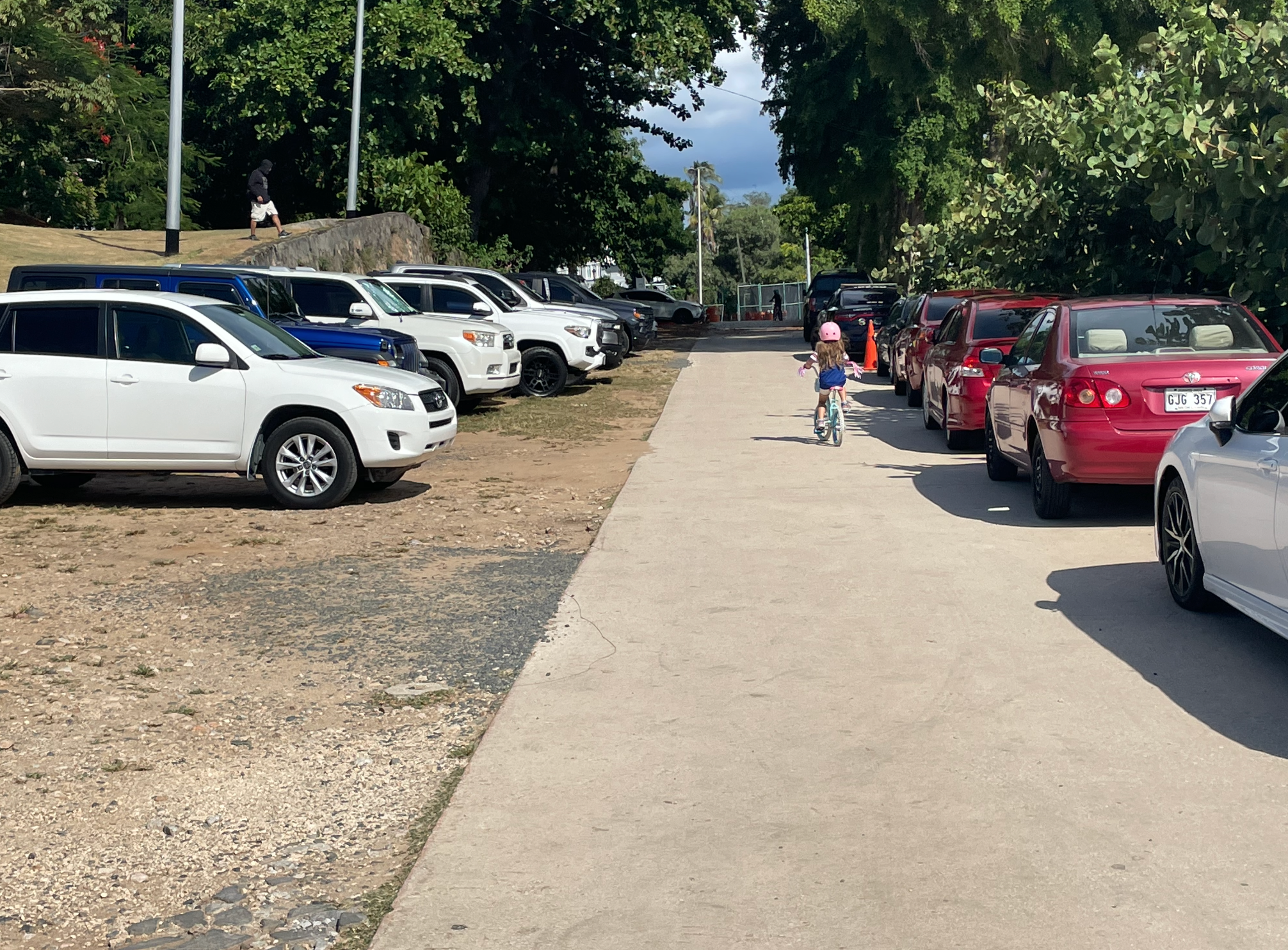 Niña en bicicleta circulando entre filas de carros estacionados cerca del Morro
